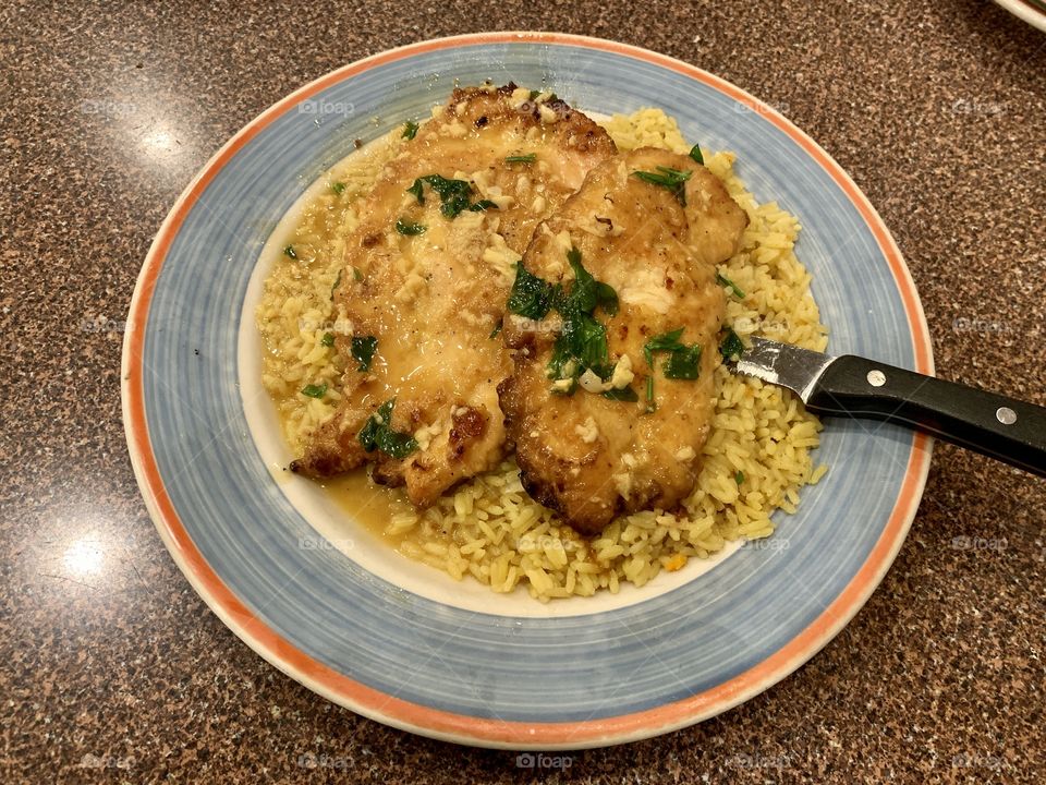 Chicken scampi with garlic sauce, yellow rice for lunch and dinner. Orange and blue round plate. 