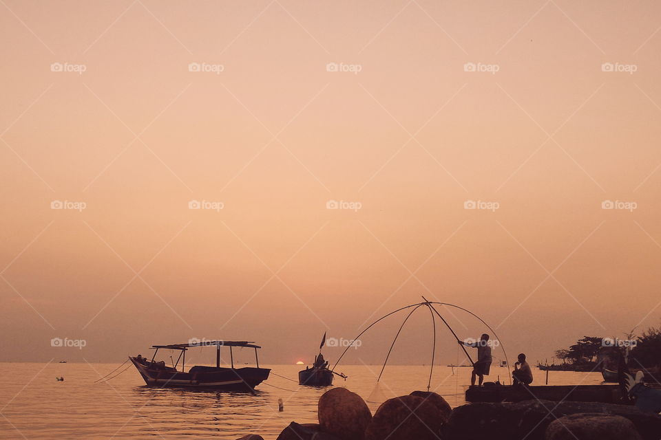 Fisherman fishing in sea during sunset