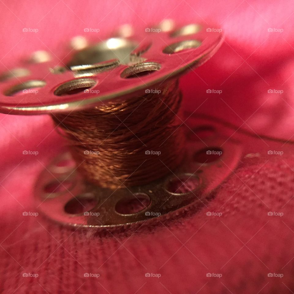 A macro view of a sewing machine bobbin with brown thread.
