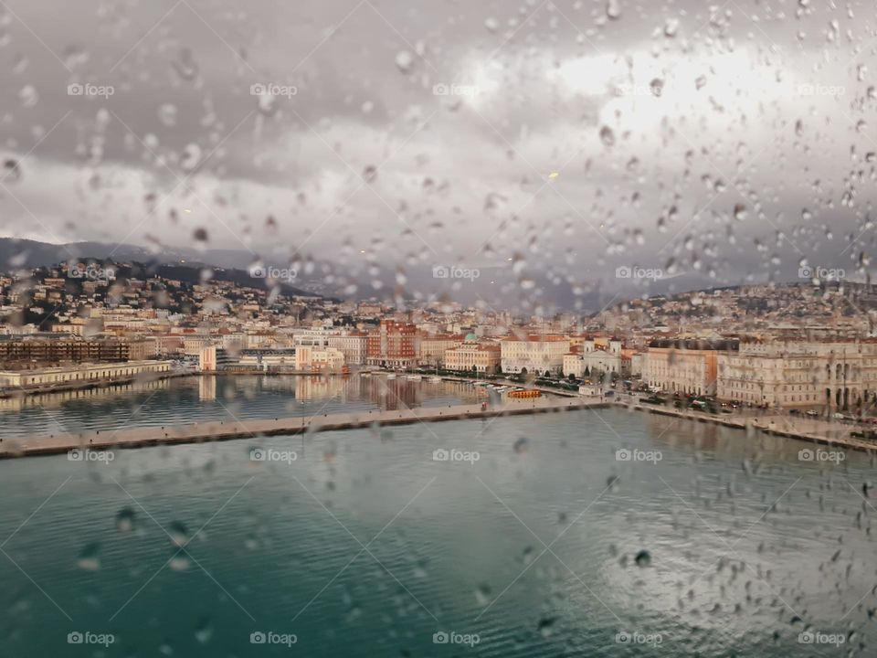 skyline of Trieste bathed by the sea, seen through a glass with raindrops