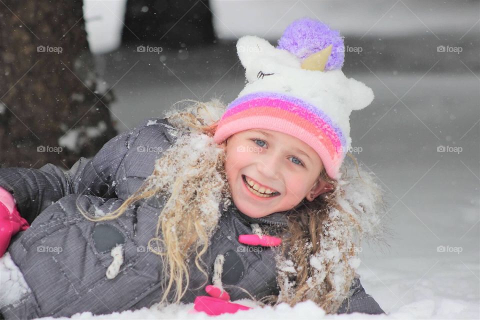 This sweet little girl is all smiles rolling around in the freshly fallen snow in her fuzzy unicorn hat. 