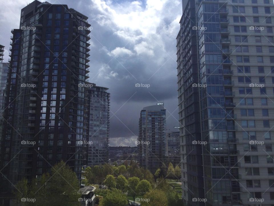 Tall Skyscrapers In Vancouver, British Columbia with Trees surrounding them and ominous clouds in the sky 