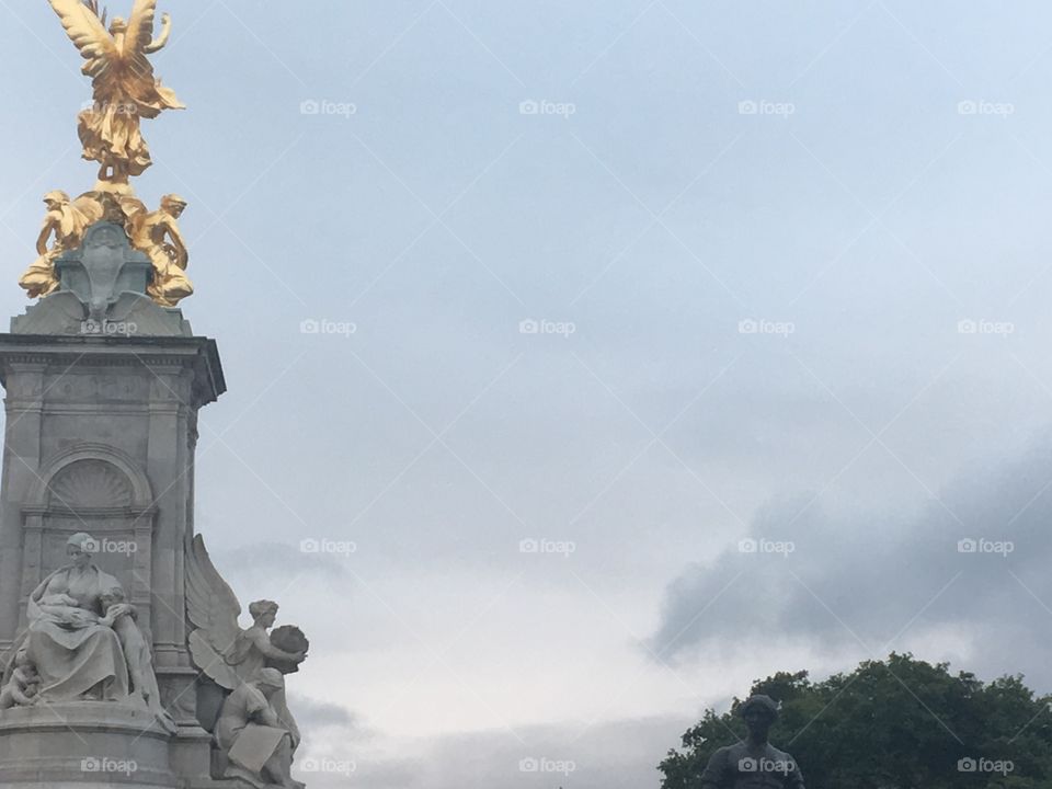 Statue outside of Buckingham Palace in London. The sun is starting to set on the cloudy day