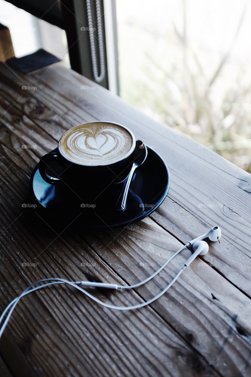 Cappuccino sitting in a window next to a pair of Apple earbud headphones. 