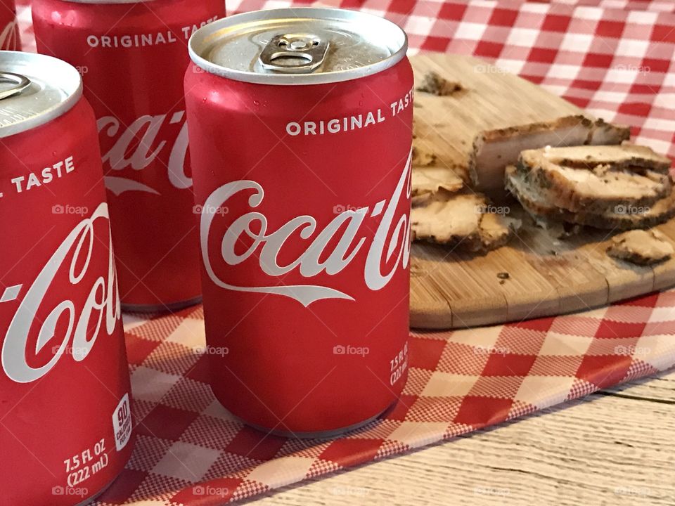 Cans of Coca-Cola on a red and white checkered background with barbecue food and potato chips 