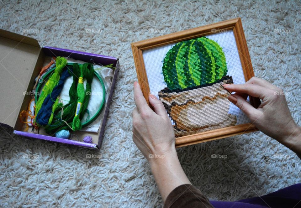 cross stitch picture of a cactus in the hands and threads for embroidery