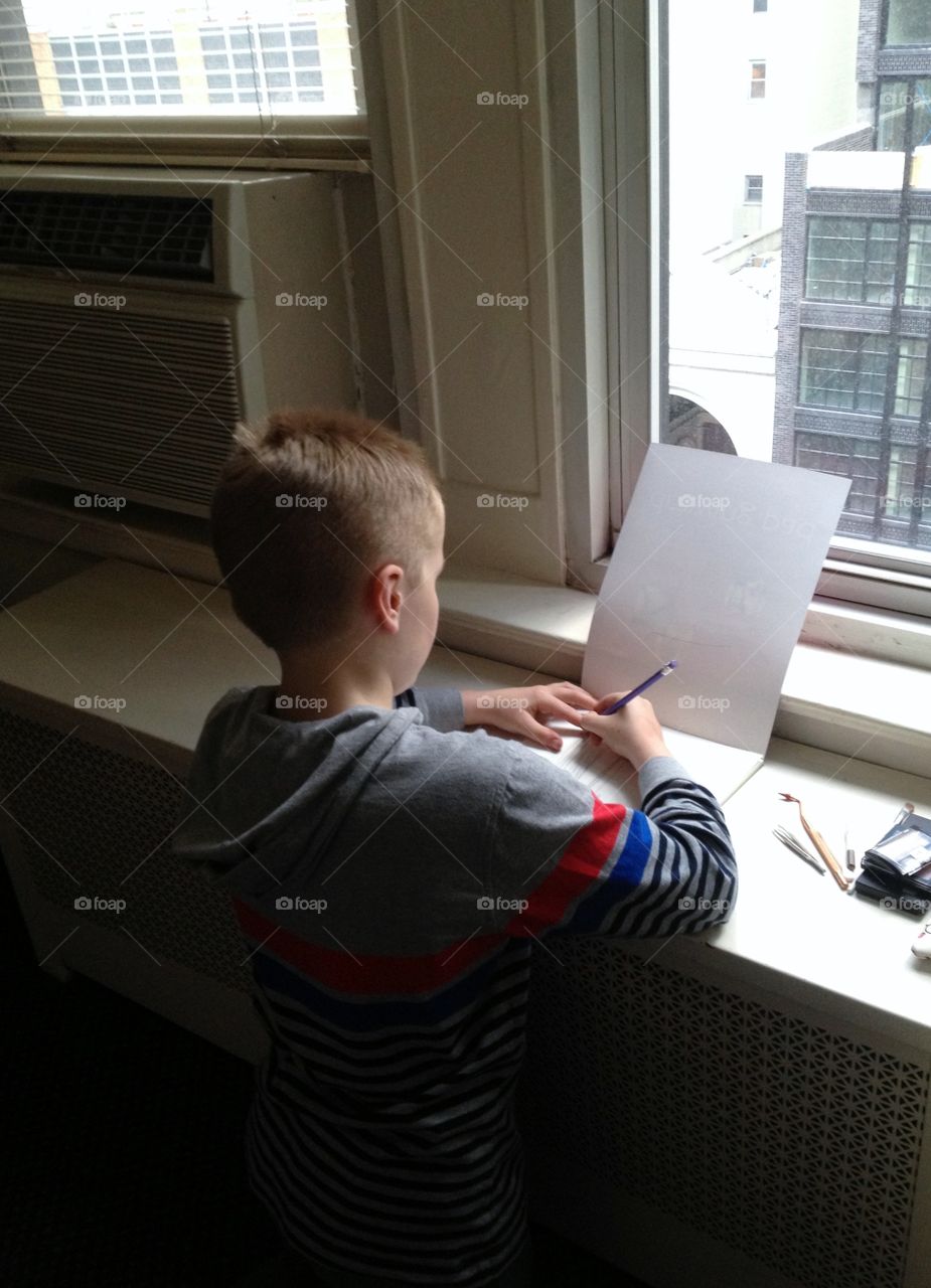 Darling photo of young boy drawing a picture with natural light streaming in through the window. 