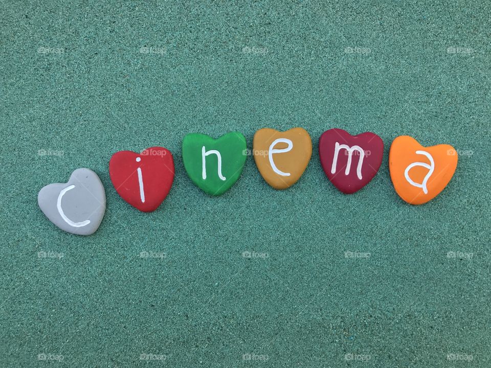 Cinema word with colored heart stones over green sand