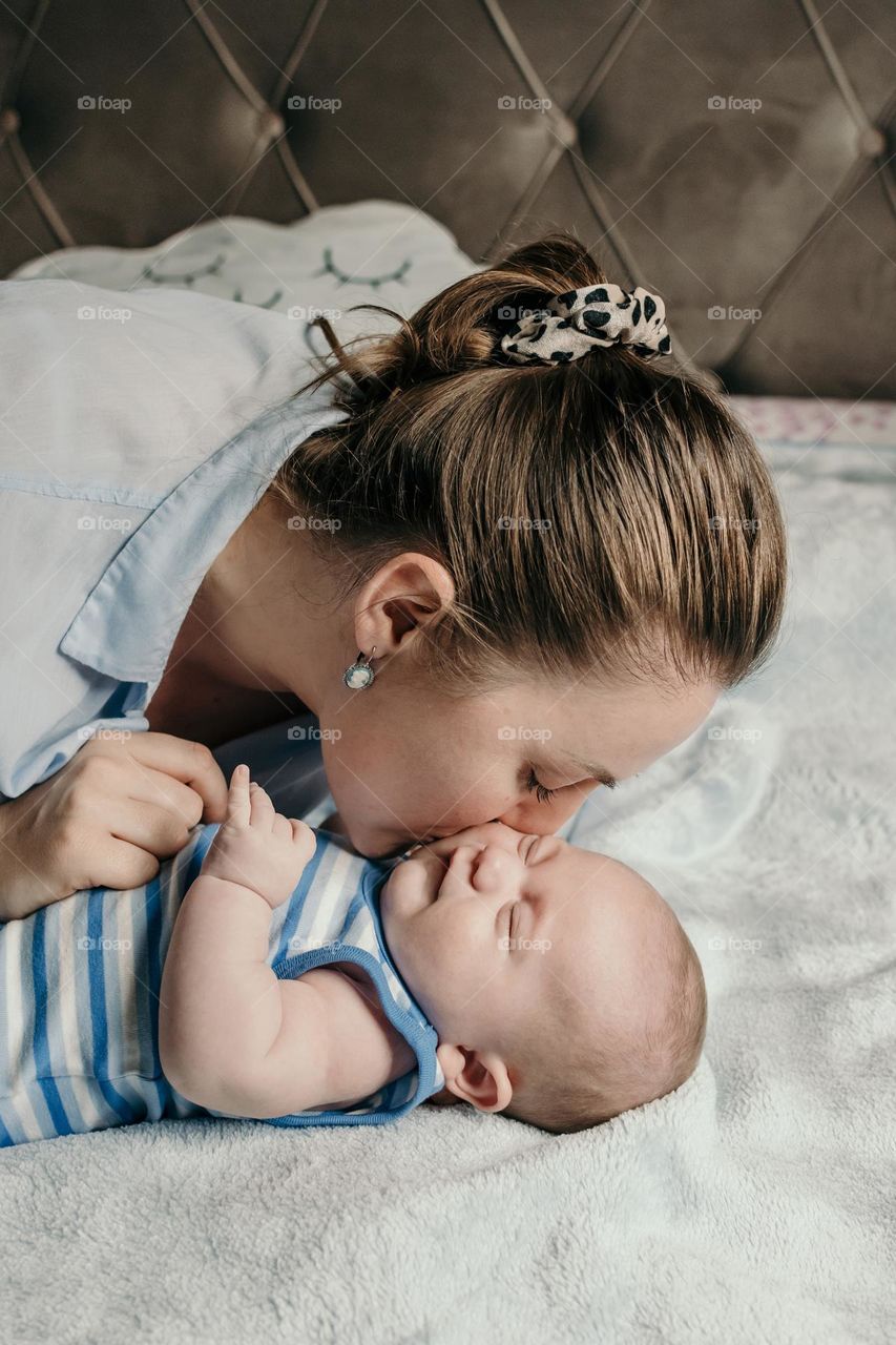 Mother kissing her baby boy on bed at home