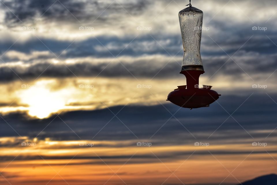 Hummingbird feeder swaying in the cold, windy night in front of a extraordinary, colourful sunset. 