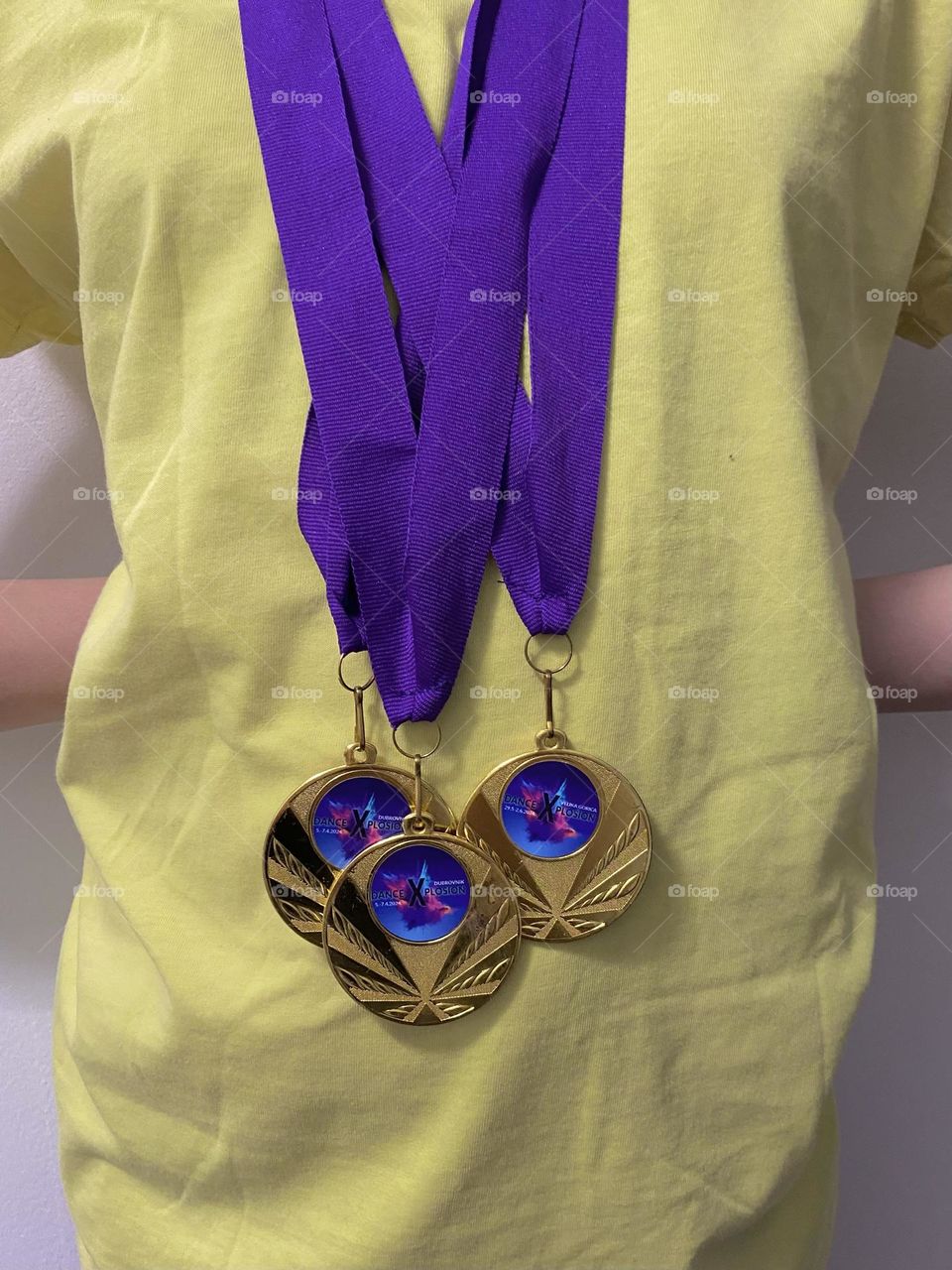 A proud winner of three gold medals. Purple ribbons against a yellow shirt.