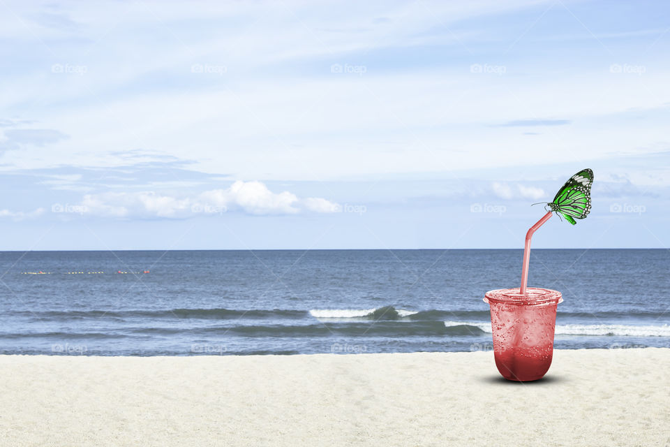 Green Butterfly on Red juice with ice in a plastic glass Background sea and the bright sky.