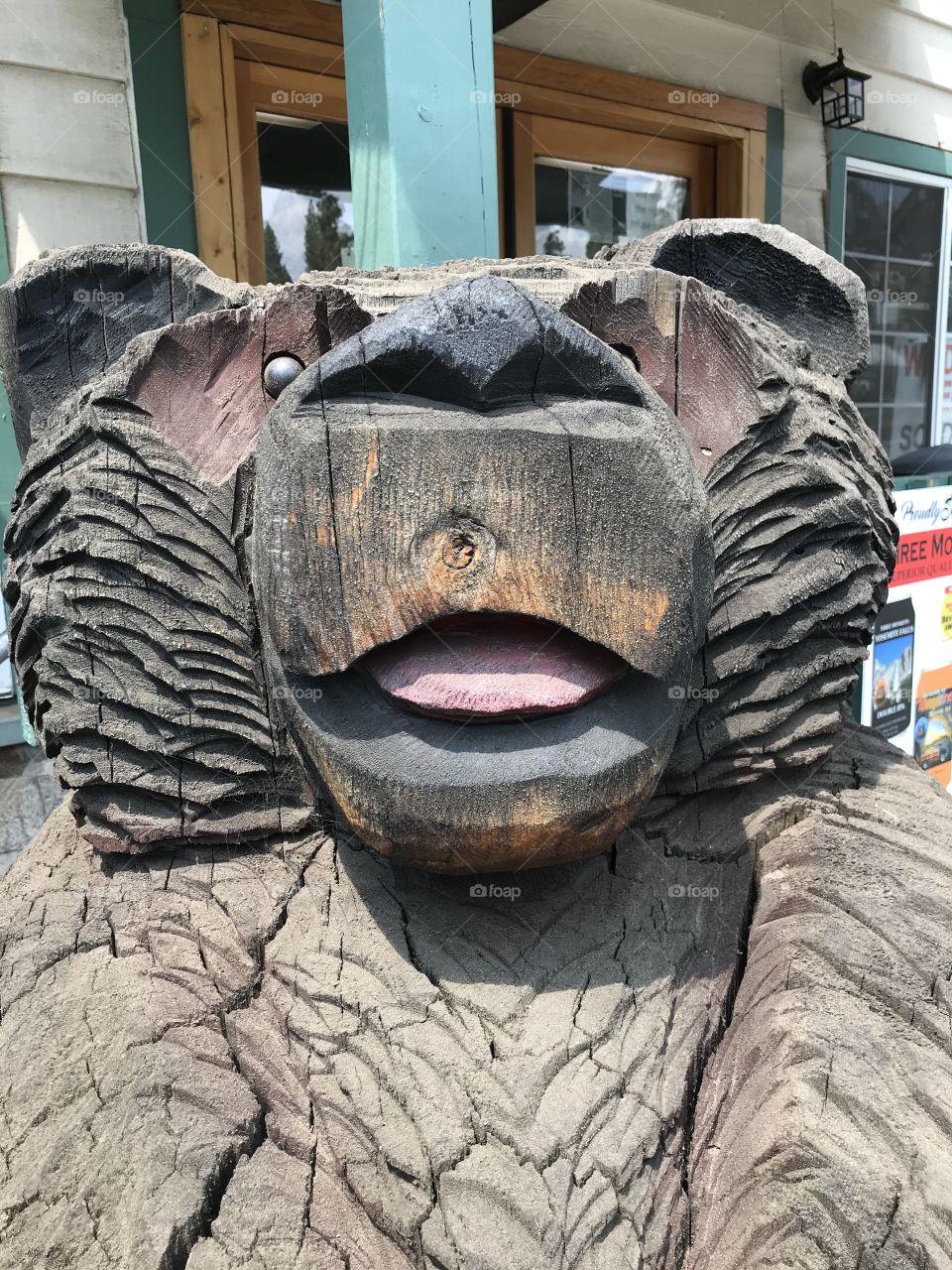 A wooden bear standing there to guard the deli and coffee shop around the clock. This is a good close-up view of him. It is getting up close and personal. π