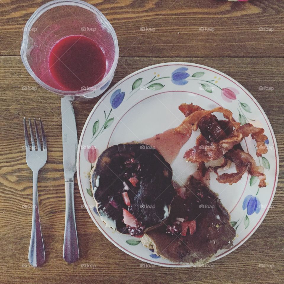 Breakfast is served. Buckwheat pancakes with berry syrup and bacon with carrot, Apple and beet juice.