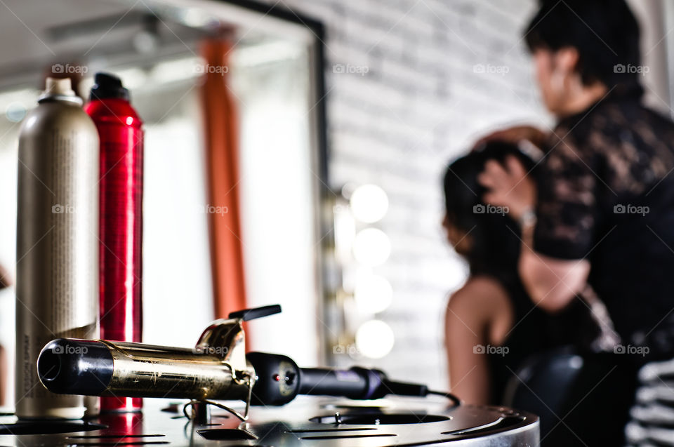 Stylist curling iron in the foreground and stylist with client in the background