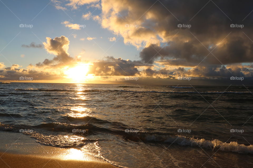 Sunset and golden clouds, waves softly crashing on the enlightened sand