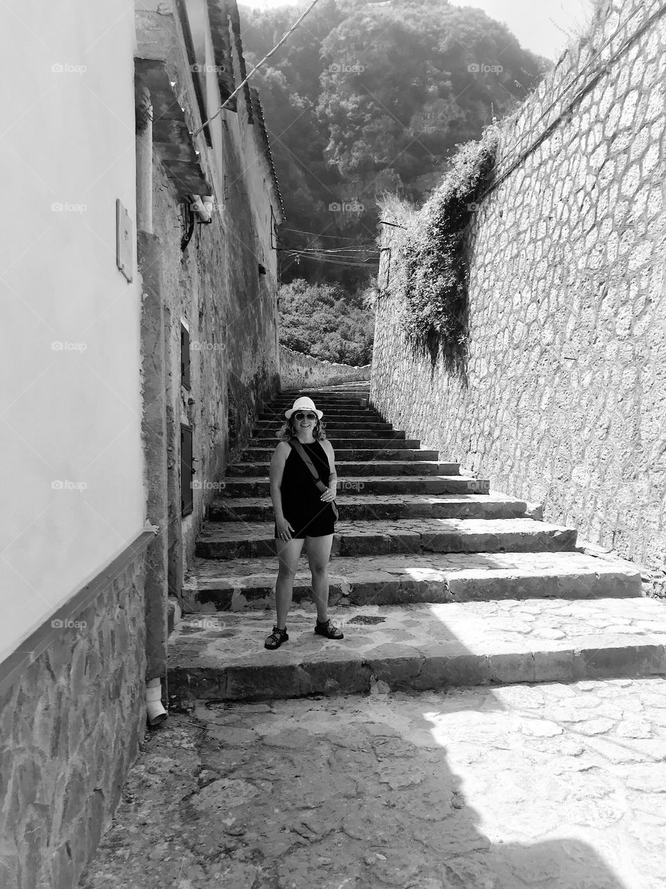 A beautiful woman poses for a photo on stone stairs up behind the town of Amalfi, Italy.