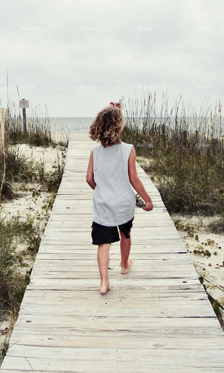 A young girl walks along a plank path towards the beach on Bald Head Island, North Carolina during summertime 