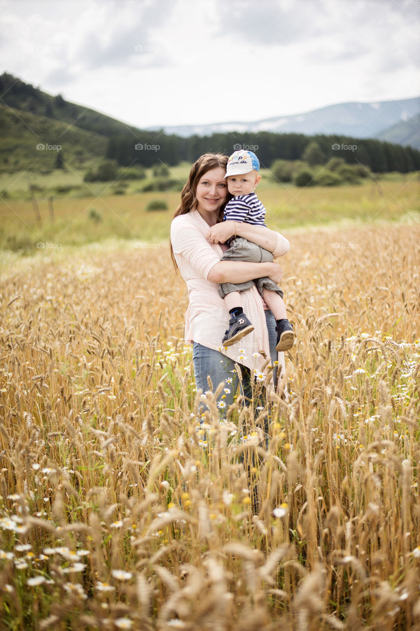 Front view of woman standing and carrying boy in field