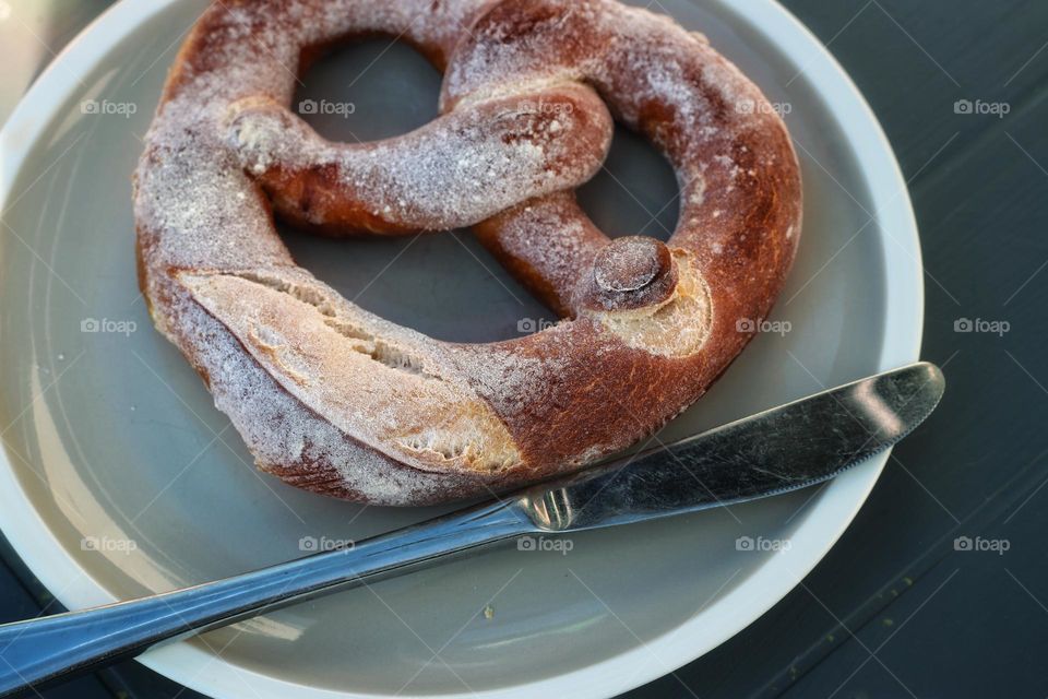 A salted pretzel and a knife lie on a gray plate 