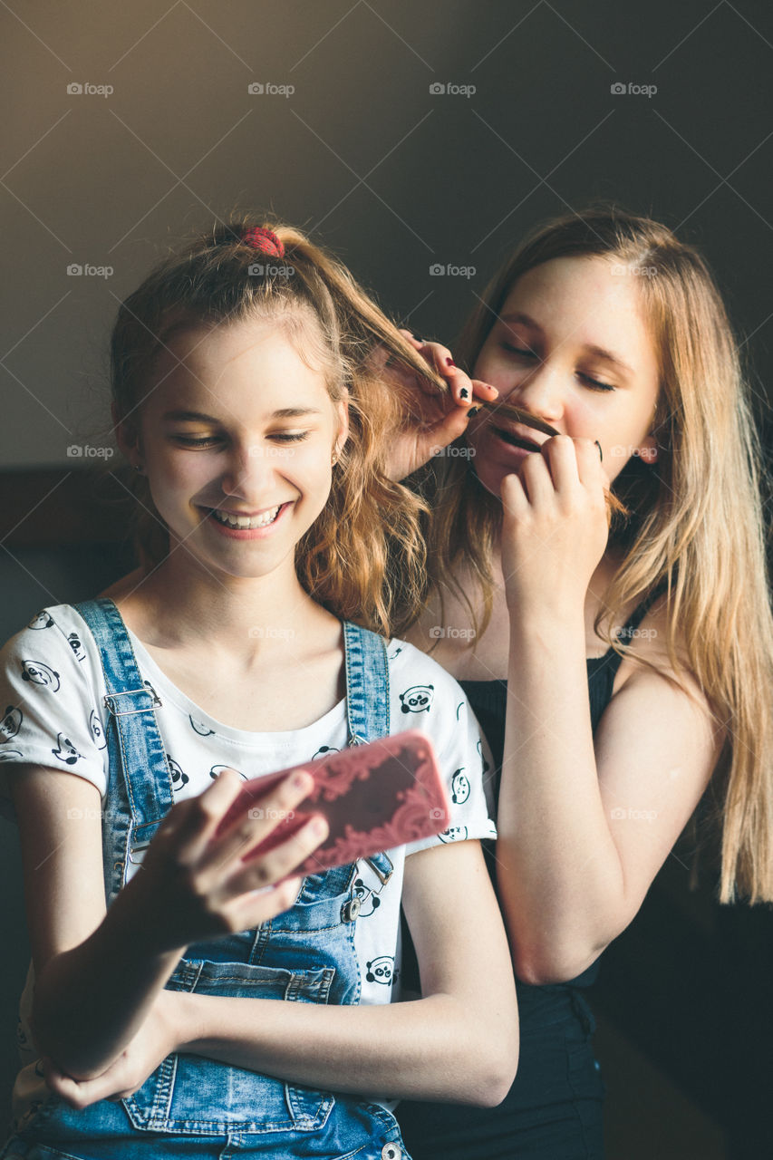 Young women taking selfie, using smartphone camera. Girls making faces, enjoying taking funny pictures together