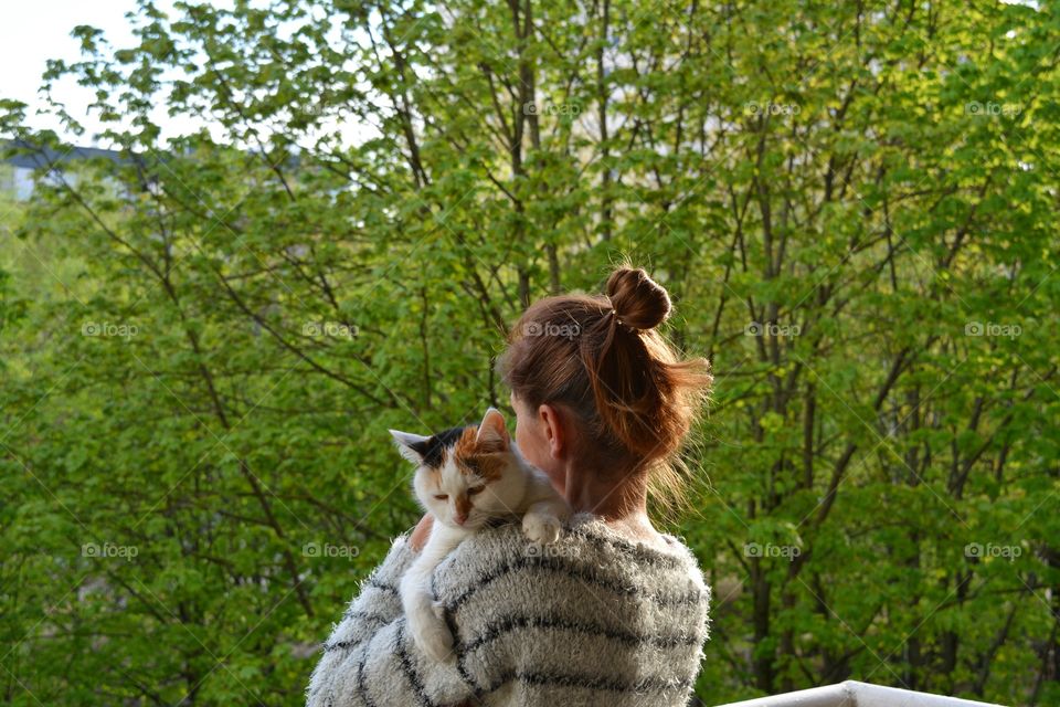 brunette girl in white sweater and white cat in the hands green background, spring and summer time, pet love