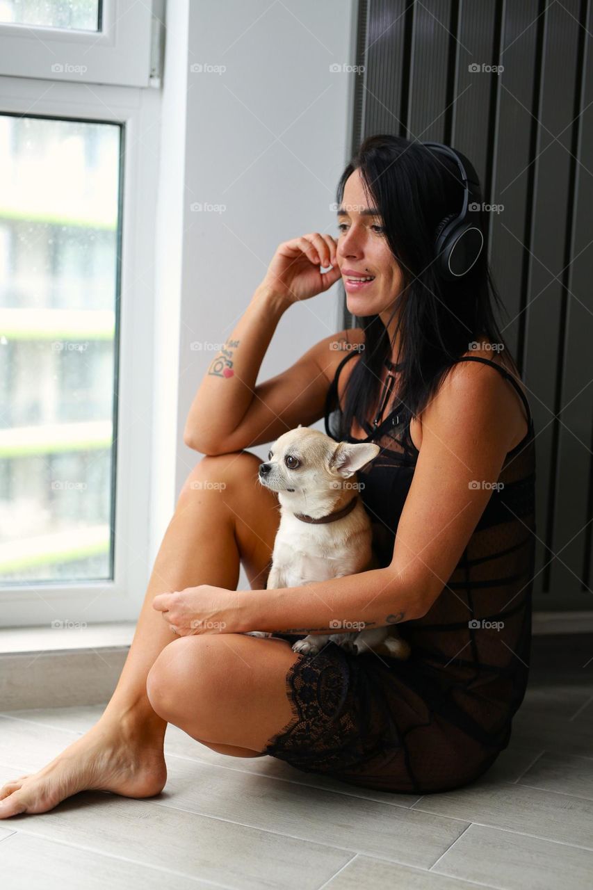 a girl in headphones, a black dress and with a dog, sits and rkna and listens to music