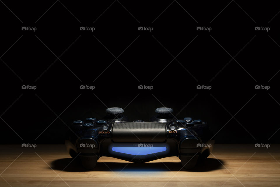 A portrait of a turned on sony PlayStation 4 controller in a spotlight with darkness around it.