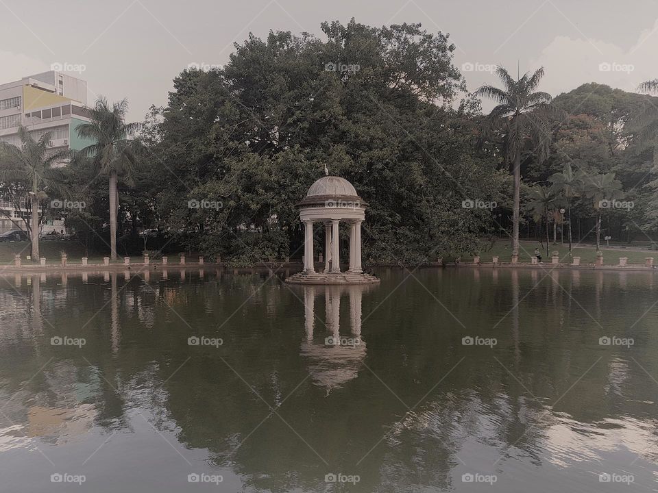 A serene lake surrounded by lush greenery, featuring a charming gazebo at its center, beautifully reflected in the water. The blend of nature, classical architecture, and the tranquil atmosphere makes this scene ideal for moments of reflection.