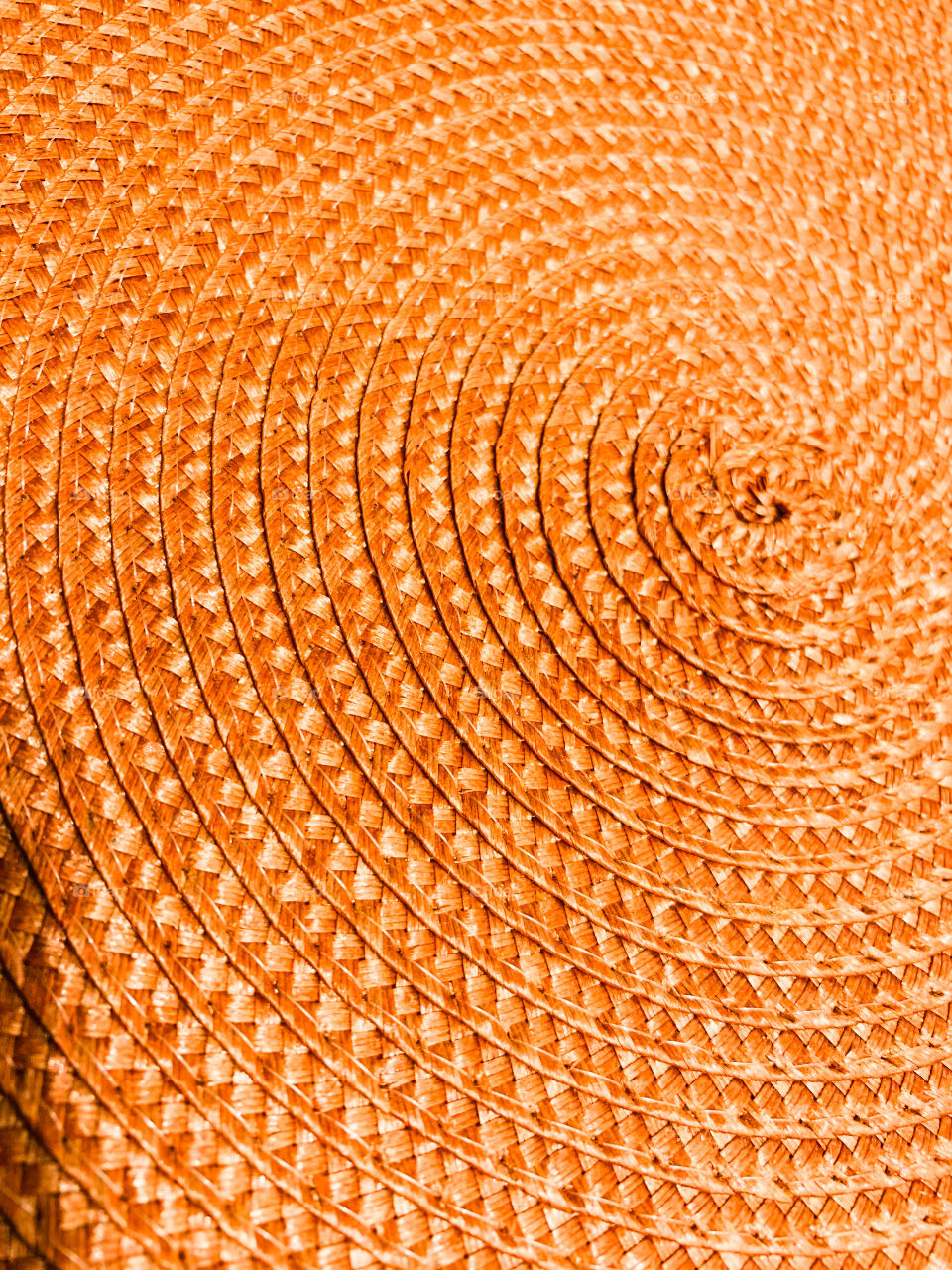 A finely crafted coiled orange tile on a table. With beautiful patterns woven with fine materials.