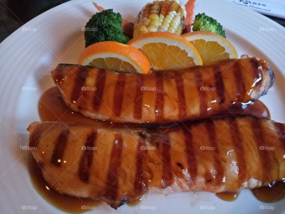 Salmon teriyaki with slice of lemon, corn, carrots and broccoli. On a white plate background.