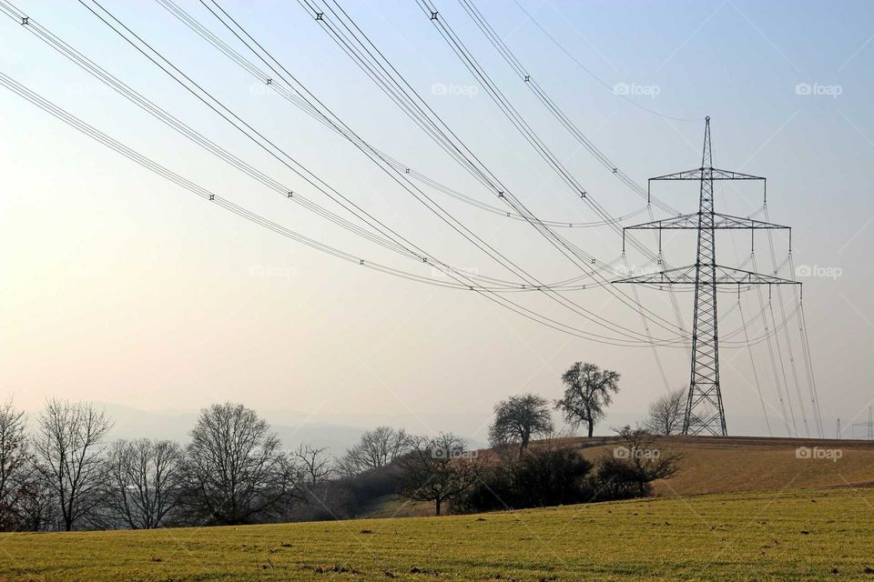 Power supply lines and an electricity Transmission tower in front of an evening sky, in winter