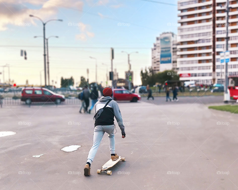 Young man skateboarding and listening to the music through the headphones in the city 