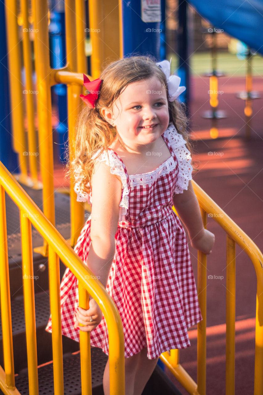 Young Girl Playing on Playground in Red Gingham Dress