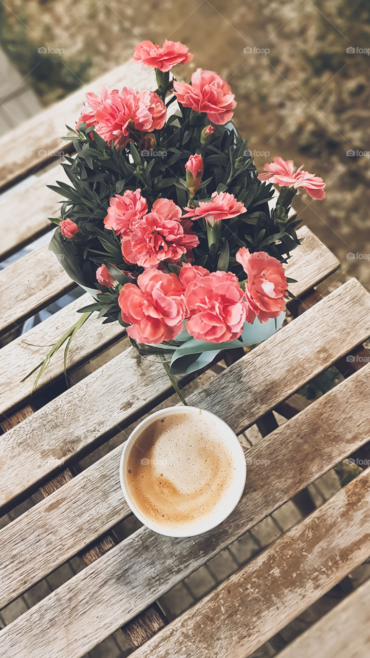 Top view of cup with cappuccino and some flowers on the wooden table.