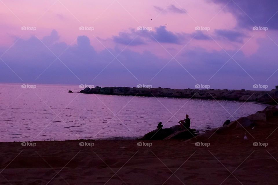 Soft pastel, lavender sunset, shades of purple and violet at Barceloneta Beach, Barcelona, Spain, person, silhouette on the rocks
