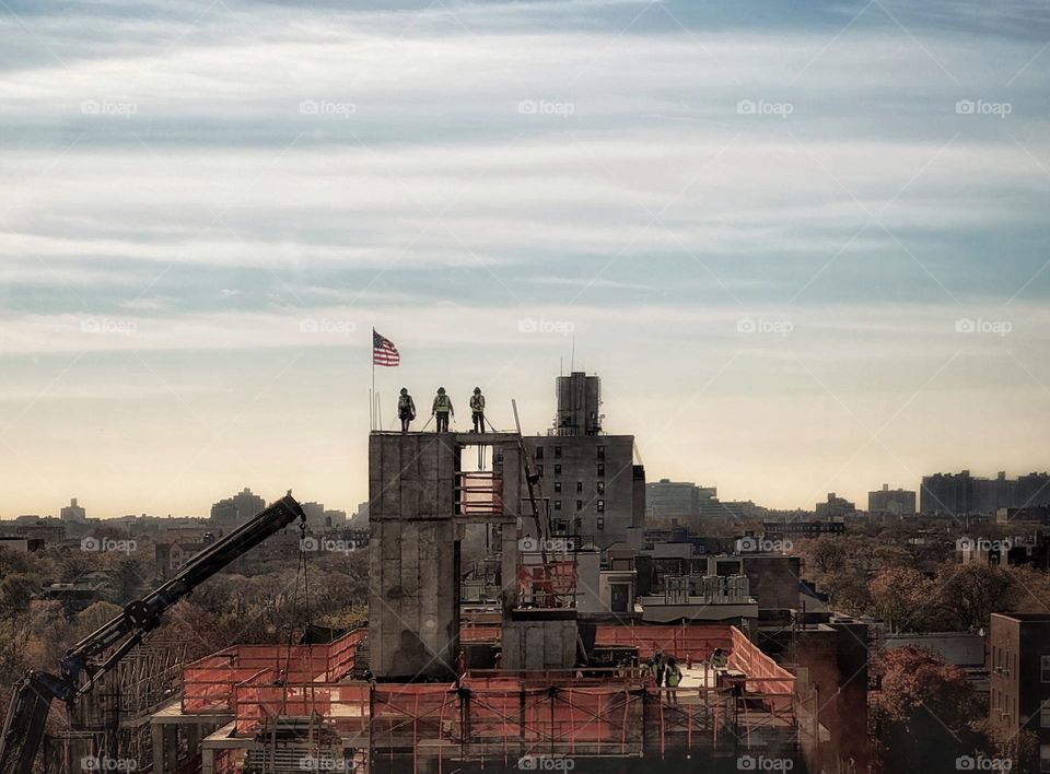 Three workers standing next to the American flag at the top of a building under construction 