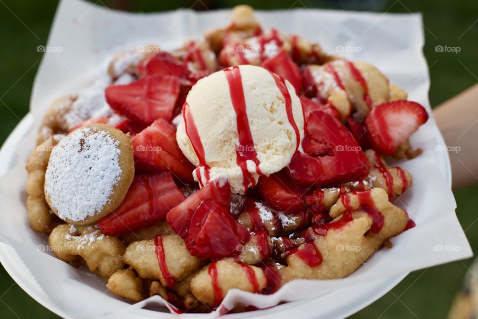 Warm,fresh funnel cake topped with strawberries and ice cream with a deep fried Oreo on the side