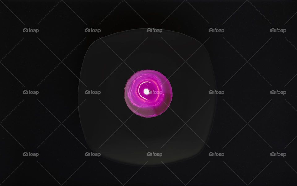 Violet burning candle on a dark dish in a black room 