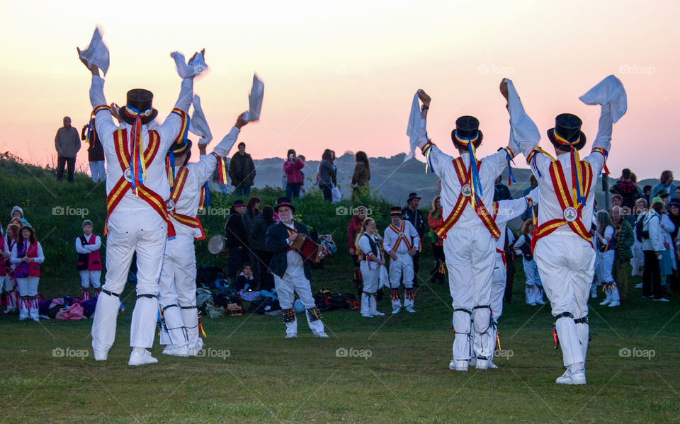 A crowd watching Morris dancers jiggle their bells and wave their hankies as the sun comes up on May 1st, near Hastings castle, UK 