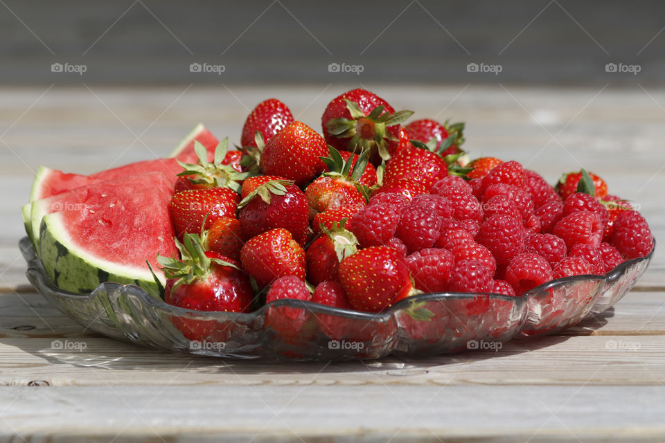 Enjoying fresh healthy strawberries raspberries watermelon on a glass plate, in June 