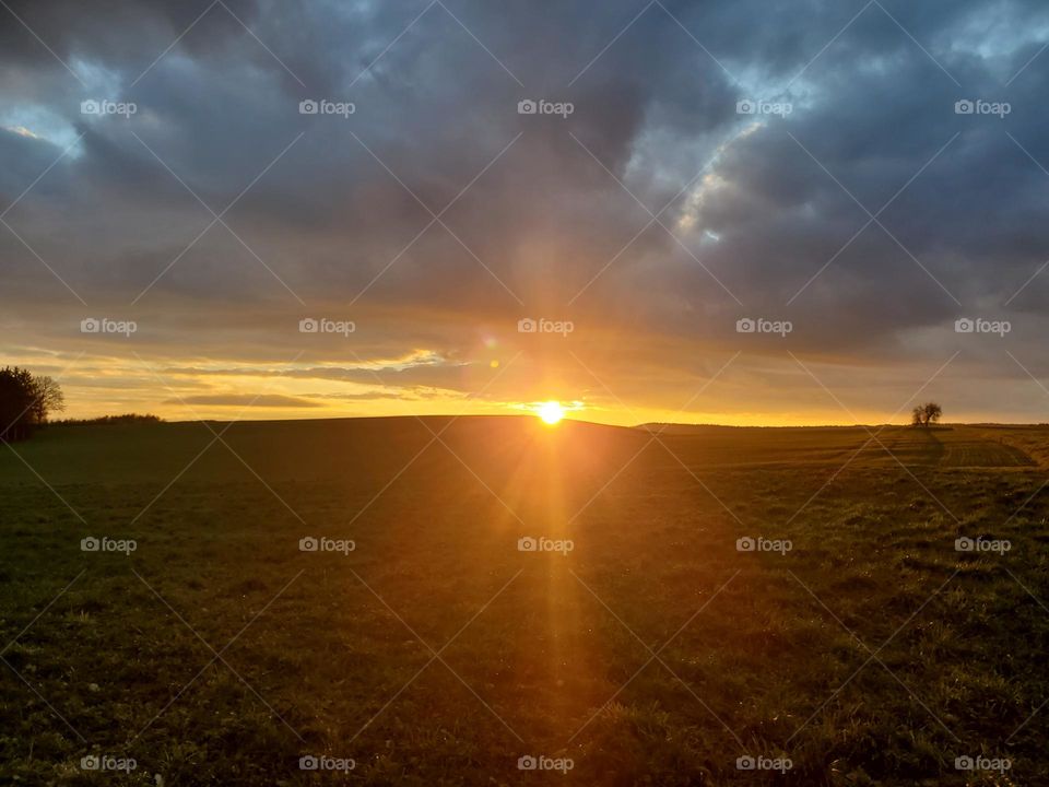 The winter sun goes down over green fields and the sky is covered by dark clouds