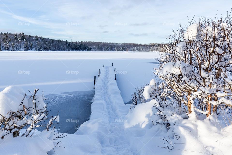 Winter wonderland, frozen lake and wooden pier covered with snow on a sunny cold winter day 