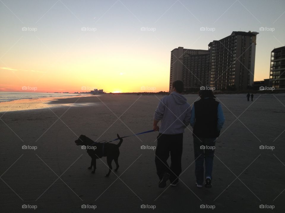 Family walking dog on beach during sunset in Winter
