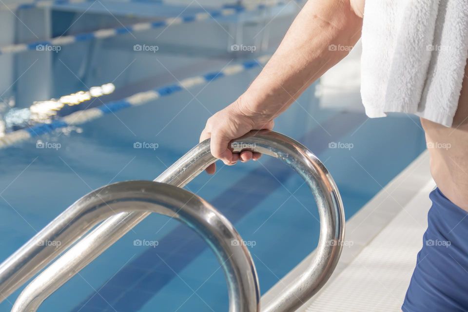 Man's hand holding onto a ladder in a swimming pool