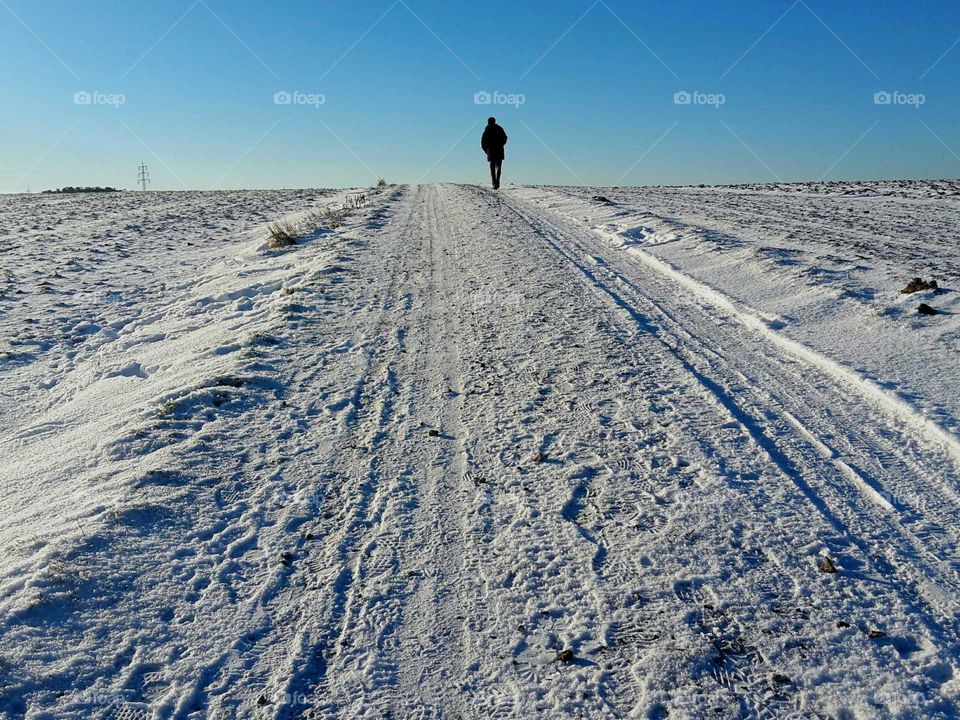 man walking up a hill in snow landscape with fields