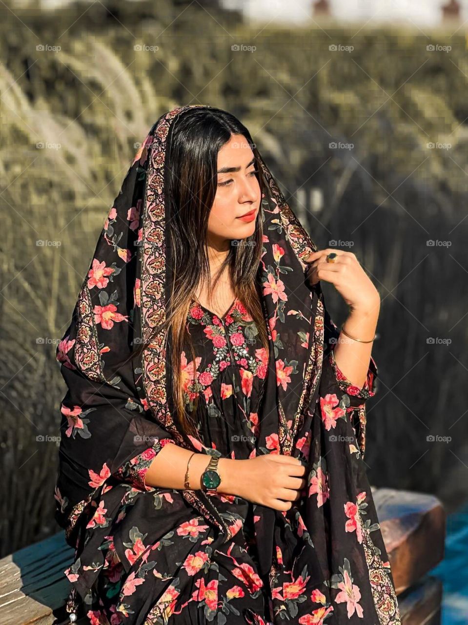 Portrait of a young woman wearing black clothes with floral motifs, sitting outdoors against a natural background