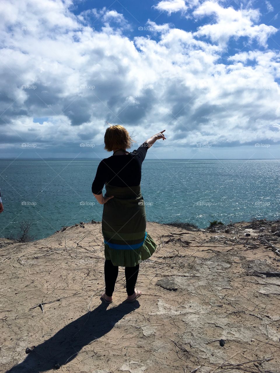 Woman on ocean cliff looking out to sea and pointing toward view