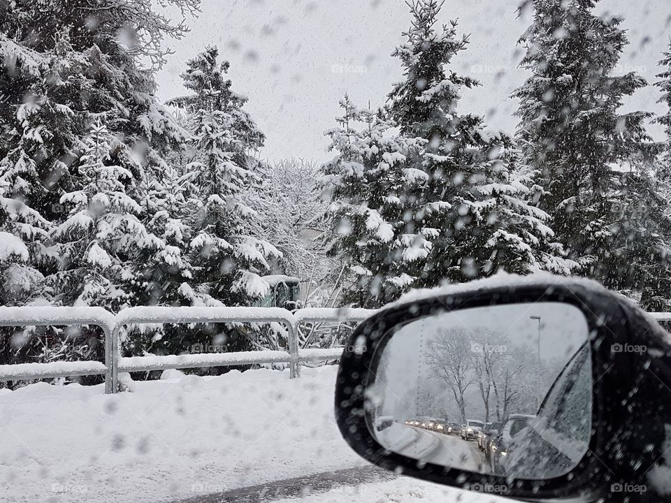 Drivning the car in snowstorm, rear view mirror, line of cars, winter 
