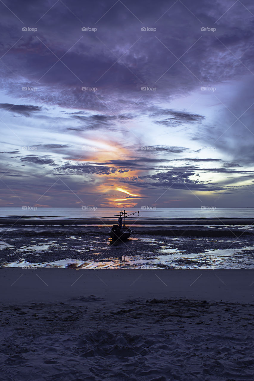 The morning sun light in the sea and the boat on the beach.